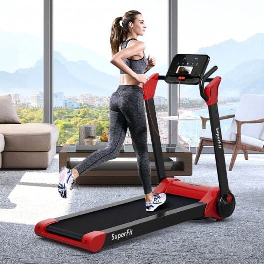 Woman using a red and black treadmill in a modern living room with large windows.